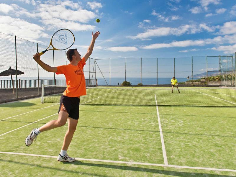 Zwei Spieler spielen Tennis auf einem sonnigen Platz mit grünem Rasen und blauem Himmel.