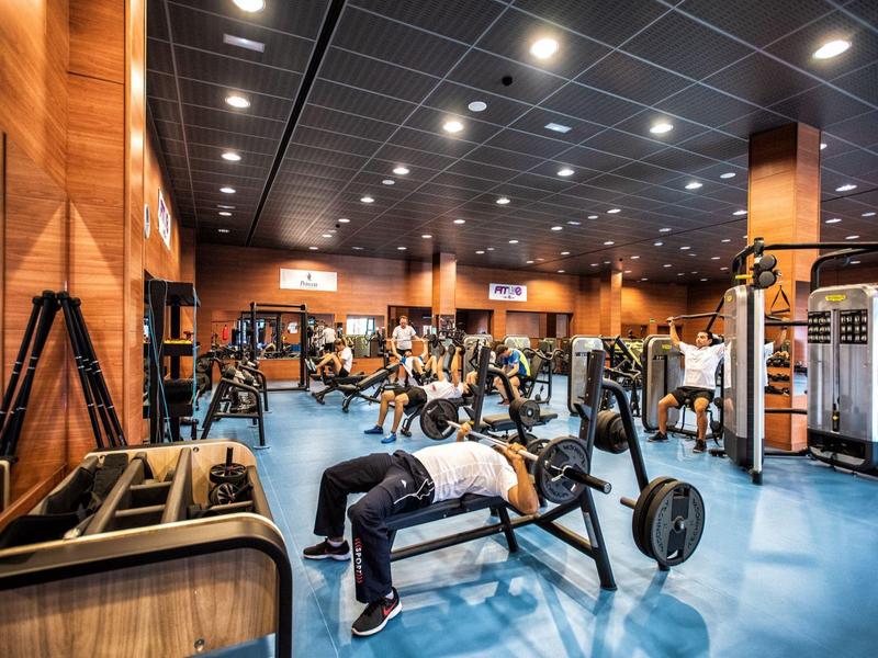 Großer Fitnessraum mit Holzverkleidung, verschiedenen Geräten und Personen beim Training.