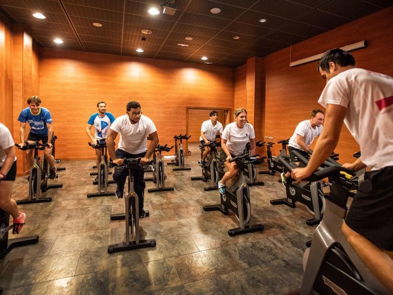 Menschen in Sportkleidung trainieren auf Spinning-Bikes in einem warm beleuchteten Raum.