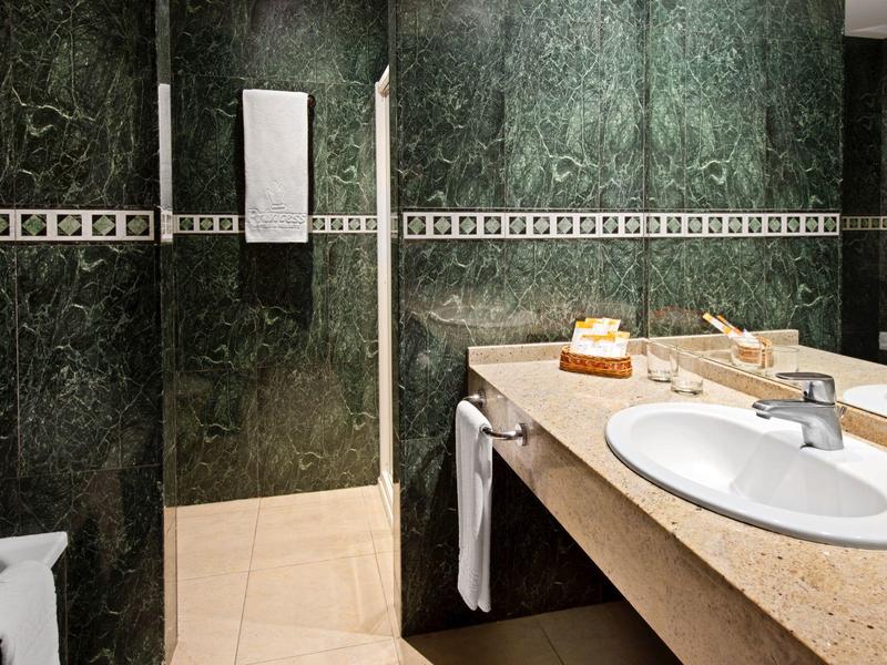 Moderner Waschraum mit grün marmorierten Wänden, beige Fliesen und großem Waschbecken auf brauner Arbeitsfläche.