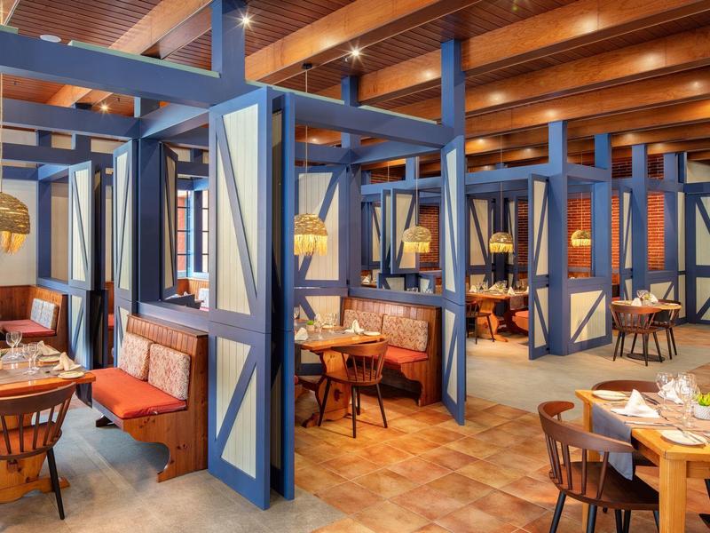 Modernes Restaurant mit Holzbalkendecke, blauen Trennwänden und gemischten Sitzplätzen aus Holz und Leder.