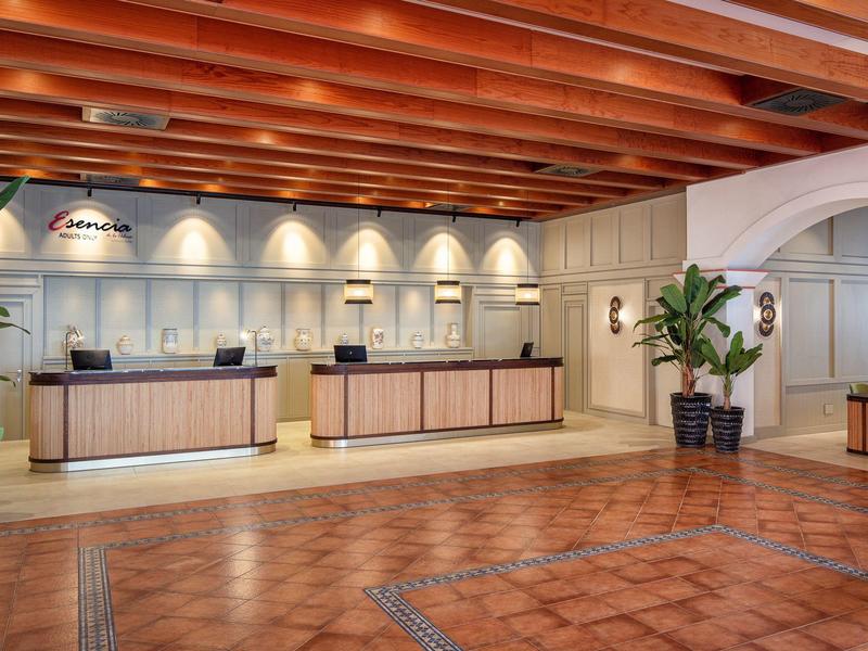 Moderne Hotelrezeption mit Holzbalkendecke, großem Tresen, Pflanzen und warmen Farben.