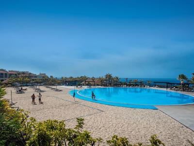 Gran piscina con área de arena alrededor y personas bajo cielo despejado