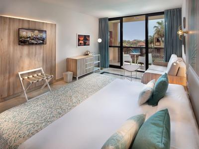 Modern hotelkamer met tweepersoonsbed, balkon en uitzicht op palmbomen en strand