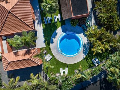 Luchtfoto van een rond zwembad omgeven door rode daken en groene palmbomen.