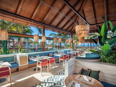 Open, modern lounge met houten plafond en comfortabele zitplaatsen in een tropische omgeving.