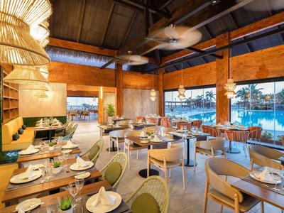 Restaurante luminoso con techo de madera, grandes ventanales y mesas elegantemente puestas junto al agua.