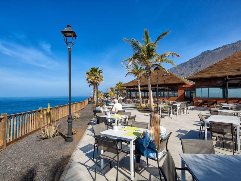 Openluchtrestaurant met tafels, stoelen, palmbomen en zeezicht bij heldere lucht