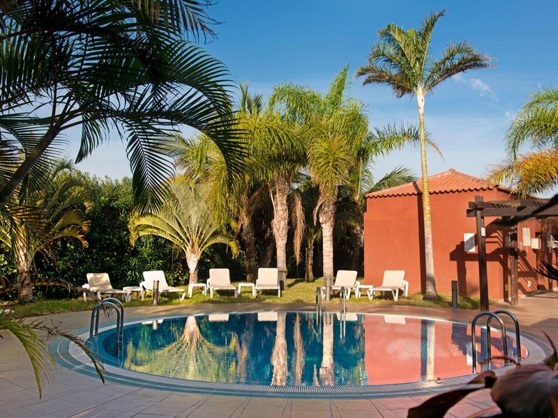 Rond zwembad met ligstoelen en palmbomen in tropische hotelsfeer bij zonsondergang.