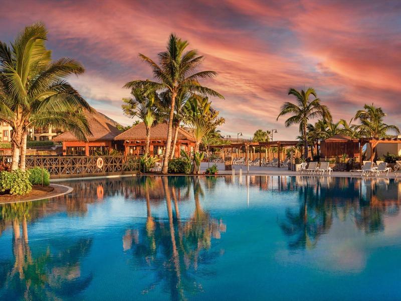 Palmboom omzoomd zwembad bij zonsondergang met hotelgebouwen op de achtergrond