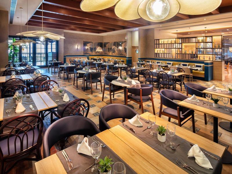 Modern restaurant met houten tafels, gedekte plaatsen en warme verlichting.