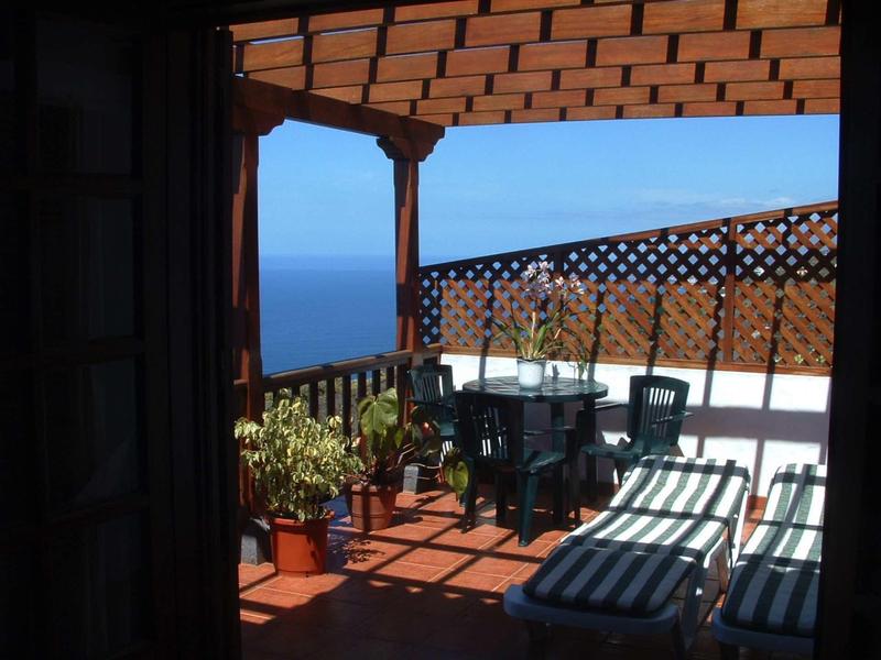 Terrazza coperta con sedie, piante e vista sul mare in una giornata soleggiata.