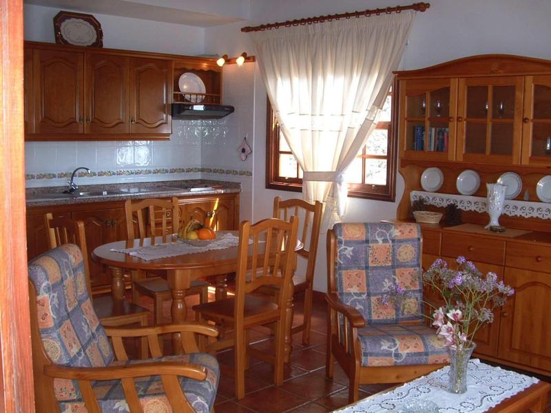 Cucina accogliente con mobili in legno, tavolo da pranzo e sedie imbottite vicino a una finestra con tenda