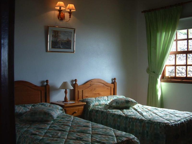 Camera d'hotel accogliente con due letti singoli, comodino e tenda verde alla finestra.