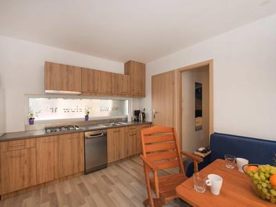 Modern kitchen area with wooden cabinets, dining area, and wooden chair in a bright room.