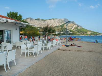 Outdoor restaurant with white tables and chairs on sandy beach overlooking mountains.
