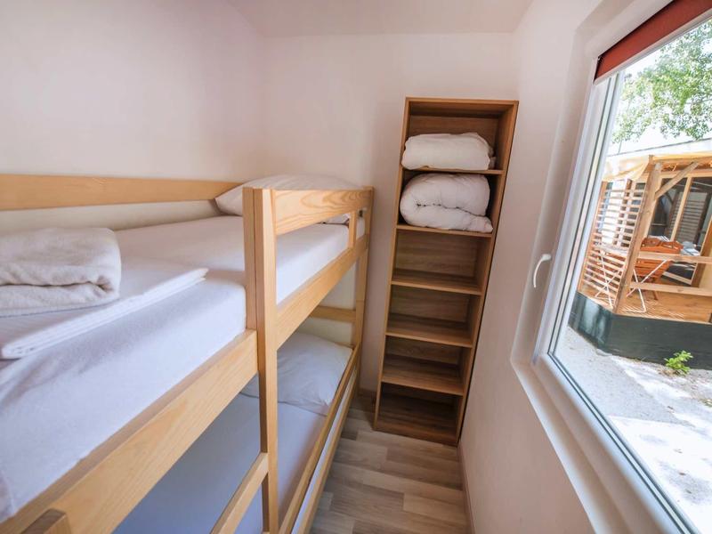Small room with bunk bed, shelving unit with bedding and window looking outside.