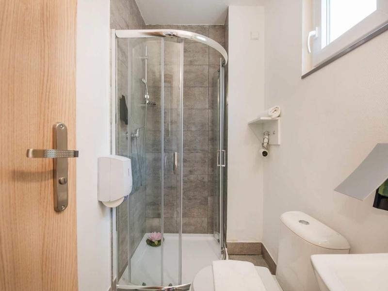 Compact bathroom with curved shower enclosure, toilet, and sink under natural light.