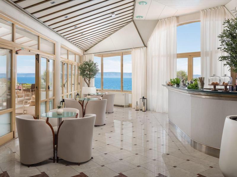 Helle Hotellobby mit großen Fenstern, Blick aufs Meer und eleganten Sitzbereichen.