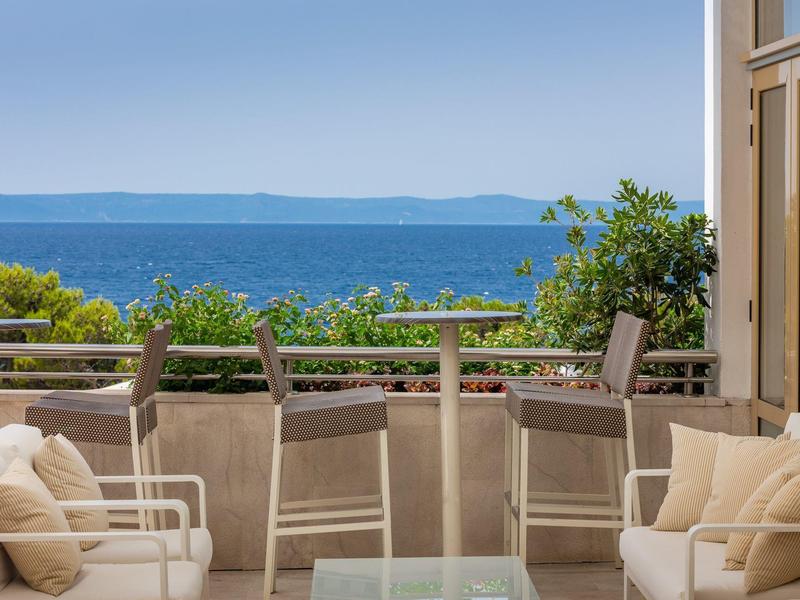 Terrasse mit gemütlichen Sesseln und Blick auf das blaue Meer und grüne Bäume.