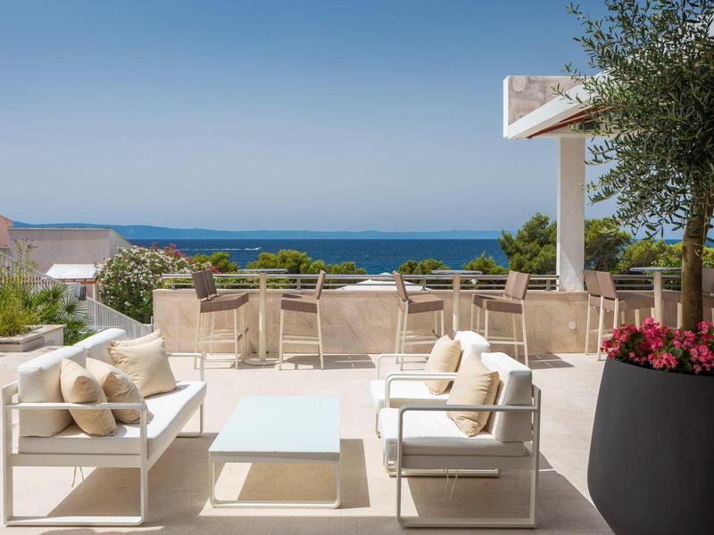 Terrasse mit weißen Sitzmöbeln und Meerblick an einem sonnigen Tag.