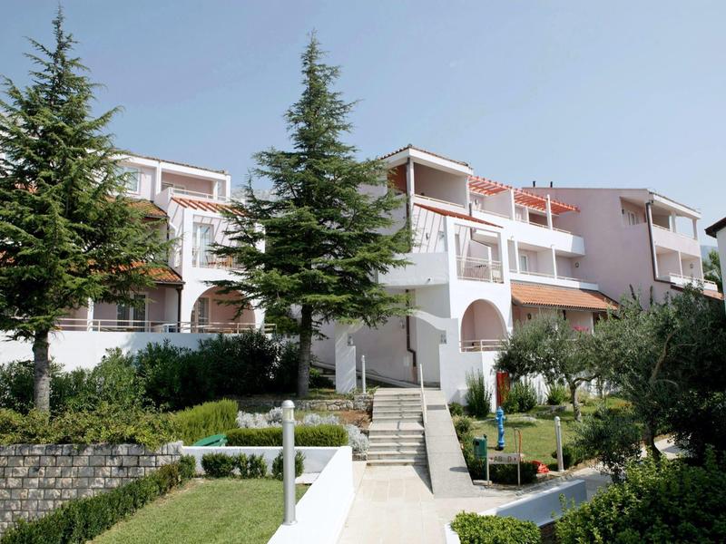 Weiße mehrstöckige Gebäude mit Grünflächen und klaren Wegen unter blauem Himmel.