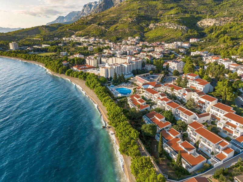 Luftaufnahme einer Küstenstadt mit Hotels, grünen Hügeln und blauem Meer.