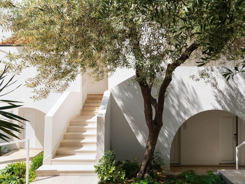 Weiße Treppe und Bogen unter einem Baum in einem sonnigen Hotelgarten.