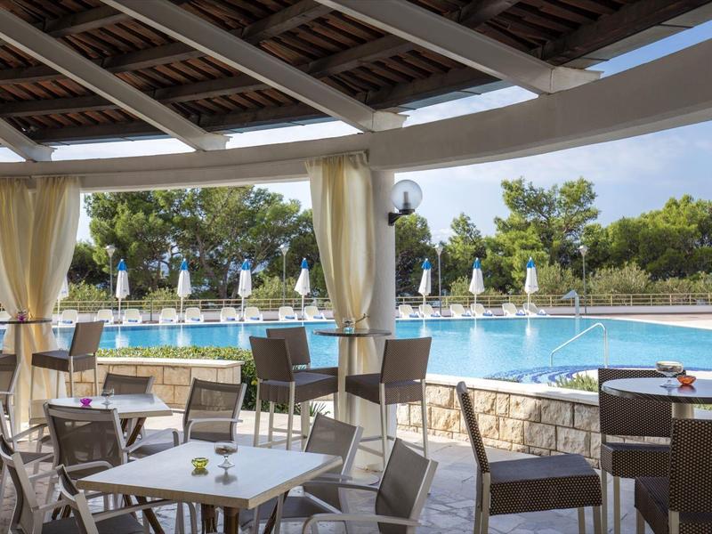 Überdachte Sitzbereiche mit Tischen und Stühlen neben einem Swimmingpool im Freien mit Sonnenschirmen.