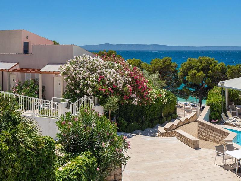 Moderner Ferienkomplex mit Pool, Liegestühlen und Meerblick in der Ferne.