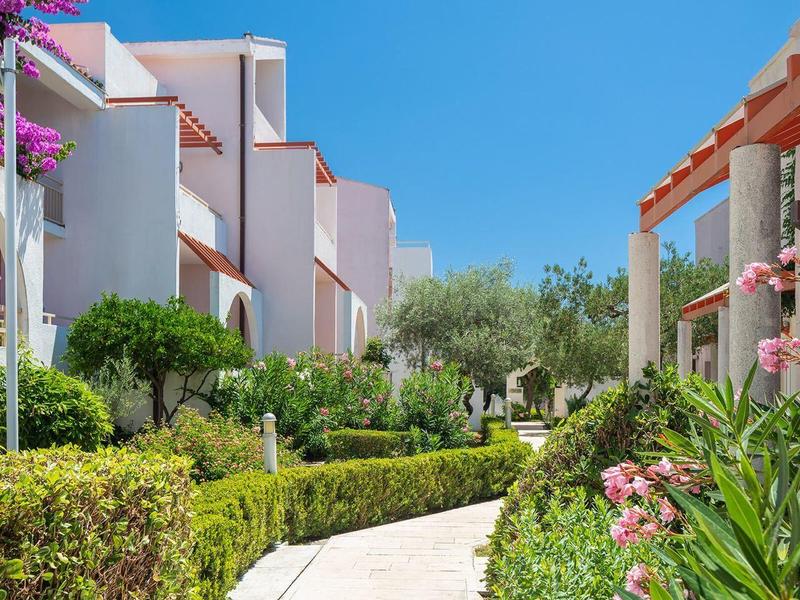 Moderne Hotelgebäude mit grünen Gärten und bunten Blumen unter klarem blauem Himmel.