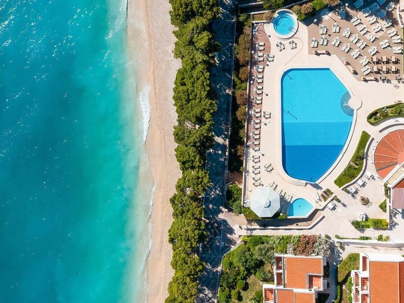 Vogelperspektive auf Resort mit Pool, Sandstrand und blauem Meer.