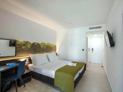 Modernes Hotelzimmer mit Doppelbett, Schreibtisch, Wand-TV und minimalistischer Dekoration.