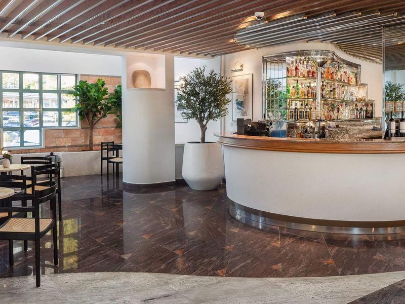 Espace bar moderne avec comptoirs blancs ronds et chaises noires dans un salon d'hôtel lumineux.