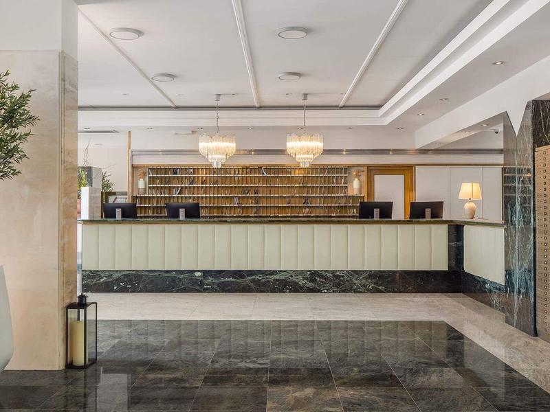 Hall d'hôtel lumineux avec réception, grandes plantes et décoration moderne.