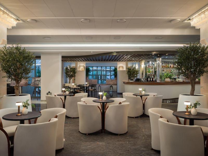 Espace bar d'hôtel élégant avec fauteuils confortables et tables rondes, décoré de plantes.