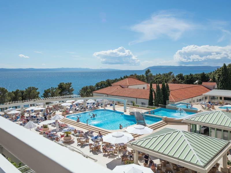 Vue depuis un balcon sur une piscine d'hôtel avec des transats et la mer en arrière-plan.