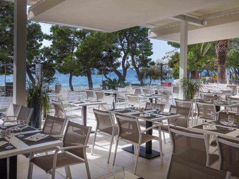 Restaurant ouvert avec des chaises et des tables donnant sur la plage et la mer en arrière-plan.