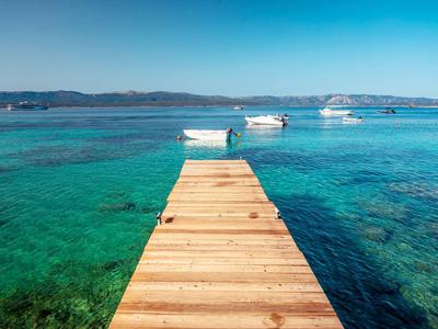 Holzsteg führt zu Booten auf klarem türkisfarbenem Meer unter blauem Himmel.