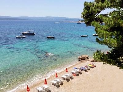Strand mit Liegestühlen, Sonnenschirmen und mehreren Booten in klarem blau-grünem Wasser