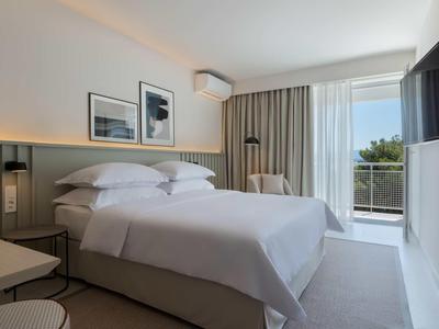 Modernes Hotelzimmer mit Doppelbett, weißen Wänden, Balkon und Fernseher an der Wand.