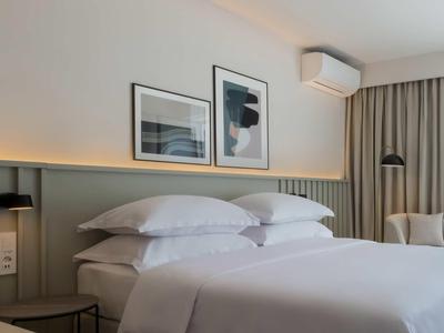 Modernes Schlafzimmer mit großem Bett, weißen Kissen, sanfter Beleuchtung und dekorativen Bildern an der Wand.