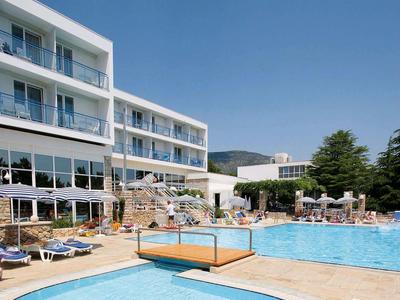 Hotelpool mit Liegestühlen und Tischen unter klarem blauem Himmel.