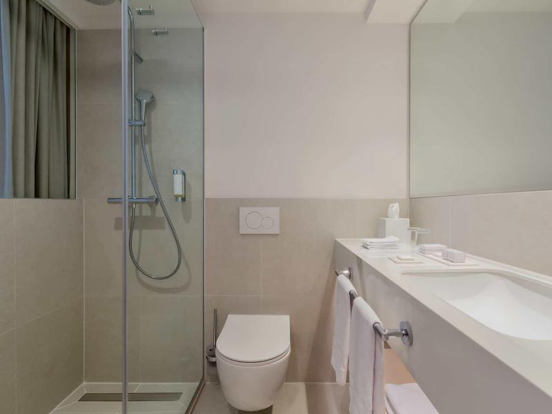 Moderner, heller Badezimmerspiegel mit Dusche, Toilette und Waschbecken, klare Linien, beige Fliesen.