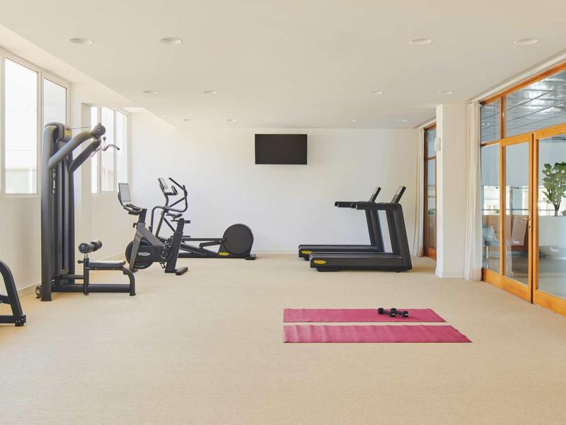 Großer heller Fitnessraum mit Geräten, zwei Laufbändern, rosafarbener Matte und Spiegelwand.