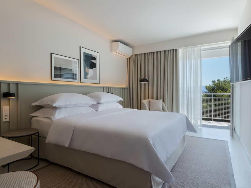 Modernes Schlafzimmer mit großem Bett, weißen Wänden, Wandbildern und Balkon mit Ausblick.