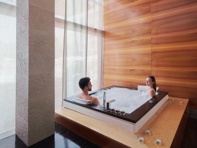 Two people relax in a modern bathtub with wood paneling and large windows.