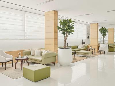 Helle Hotellobby mit modernen Sitzgruppen, großen Pflanzen und minimalistischer Inneneinrichtung.