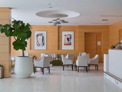 Modern hotel lounge area with comfortable armchairs, artwork, and large indoor plant.