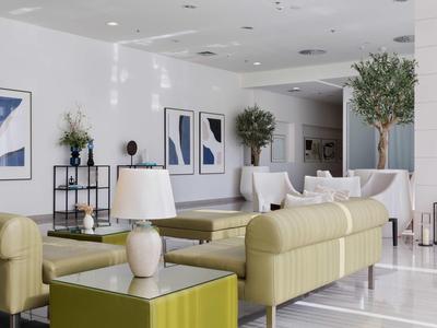 Moderner Hotel-Loungebereich mit beigen Sofas, grünem Couchtisch und abstrakter Wandkunst.